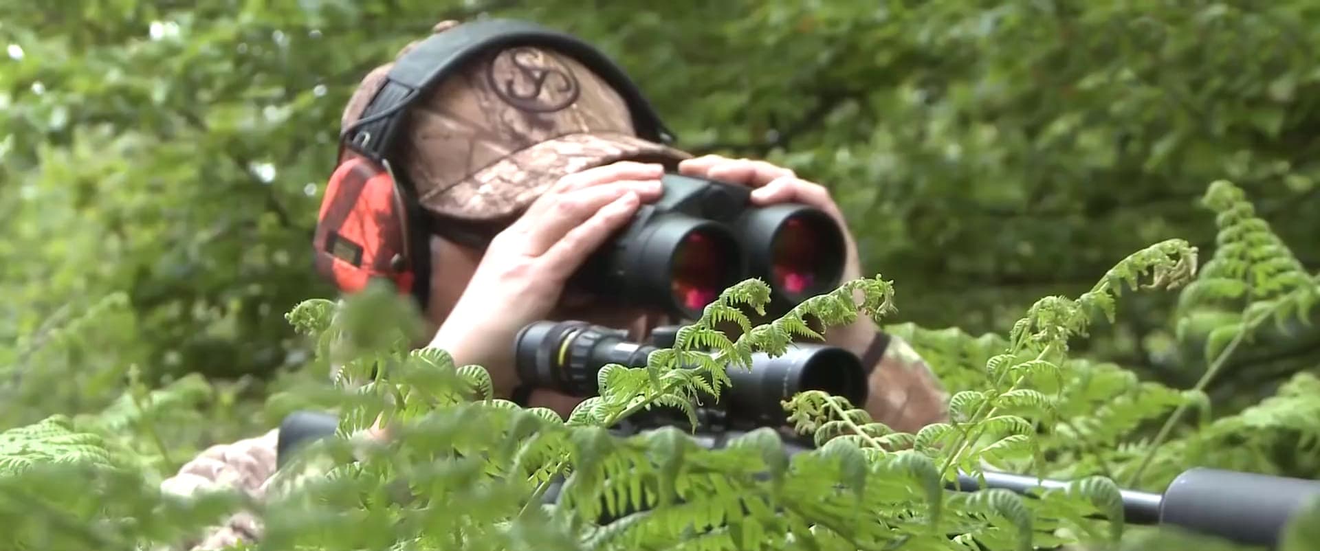 A hunter glassing a timbered basin with binoculars in flat morning light